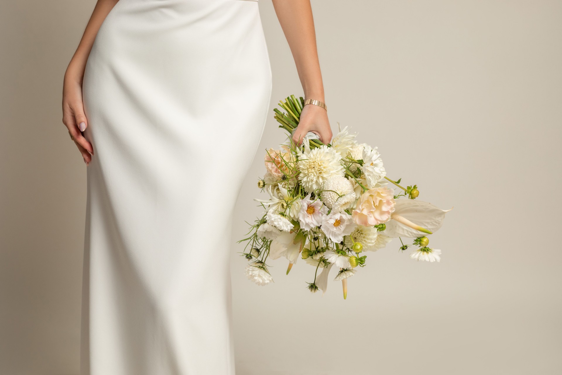 Nicht erkennbare verkürzte Frau in weißem elegantem Seidenkleid mit weißem Strauß natürlicher Blumen in der Hand mit Accessoires